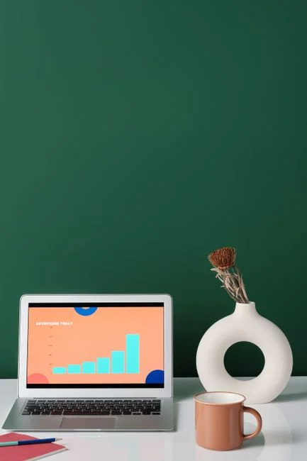 Un espace de travail contemporain où des mains examinent des données marketing sur un ordinateur portable et des documents papier.